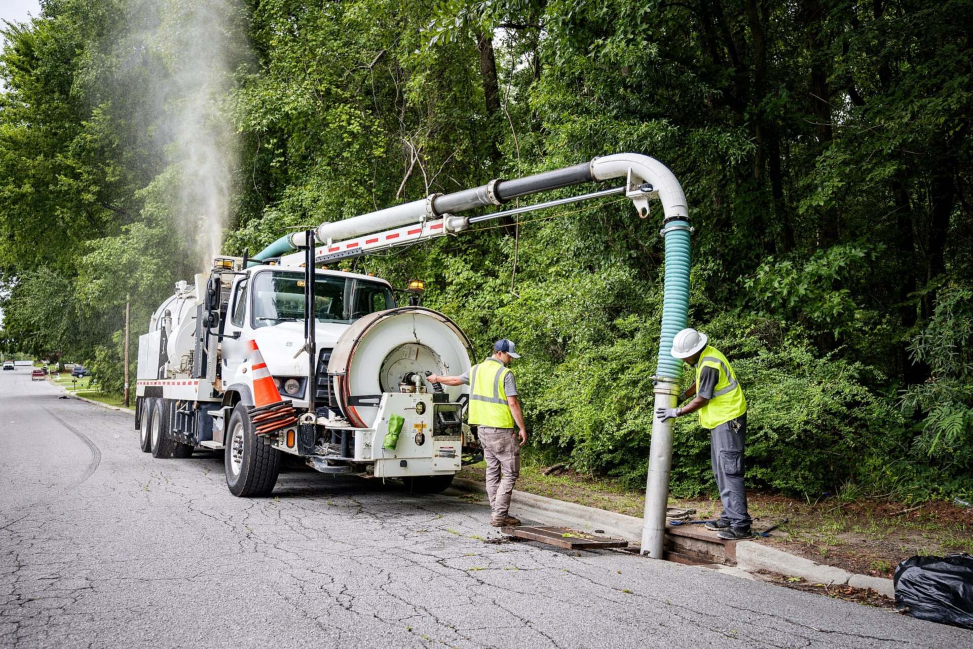 Combination vacuum truck with its boom over a storm drain while a crew in safety vests works the hose