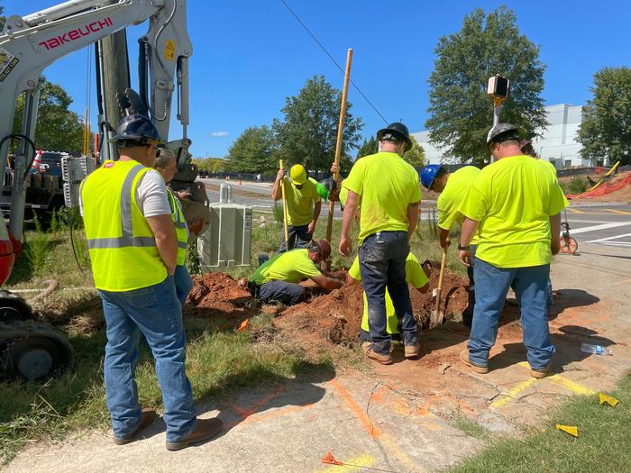 Utility crew digging at a street corner with orange locate paint and marker flags on the ground