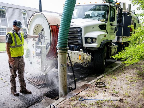 Operator at the hose reel of a vacuum truck with the suction tube down in a curbside catch basin