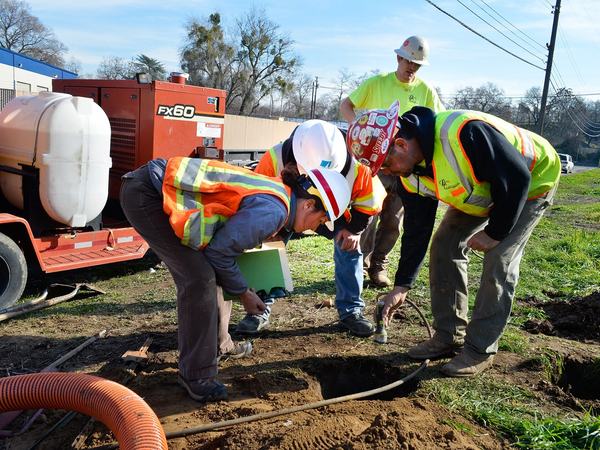 Crew in hard hats checking a small pothole dug to locate a buried gas line